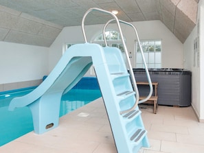 A swimming pool with a blue slide and a ladder, a hot tub, and a view of the outdoors through a window. - 4 Star Holiday Home in Ulfborg (Ulfborg)
