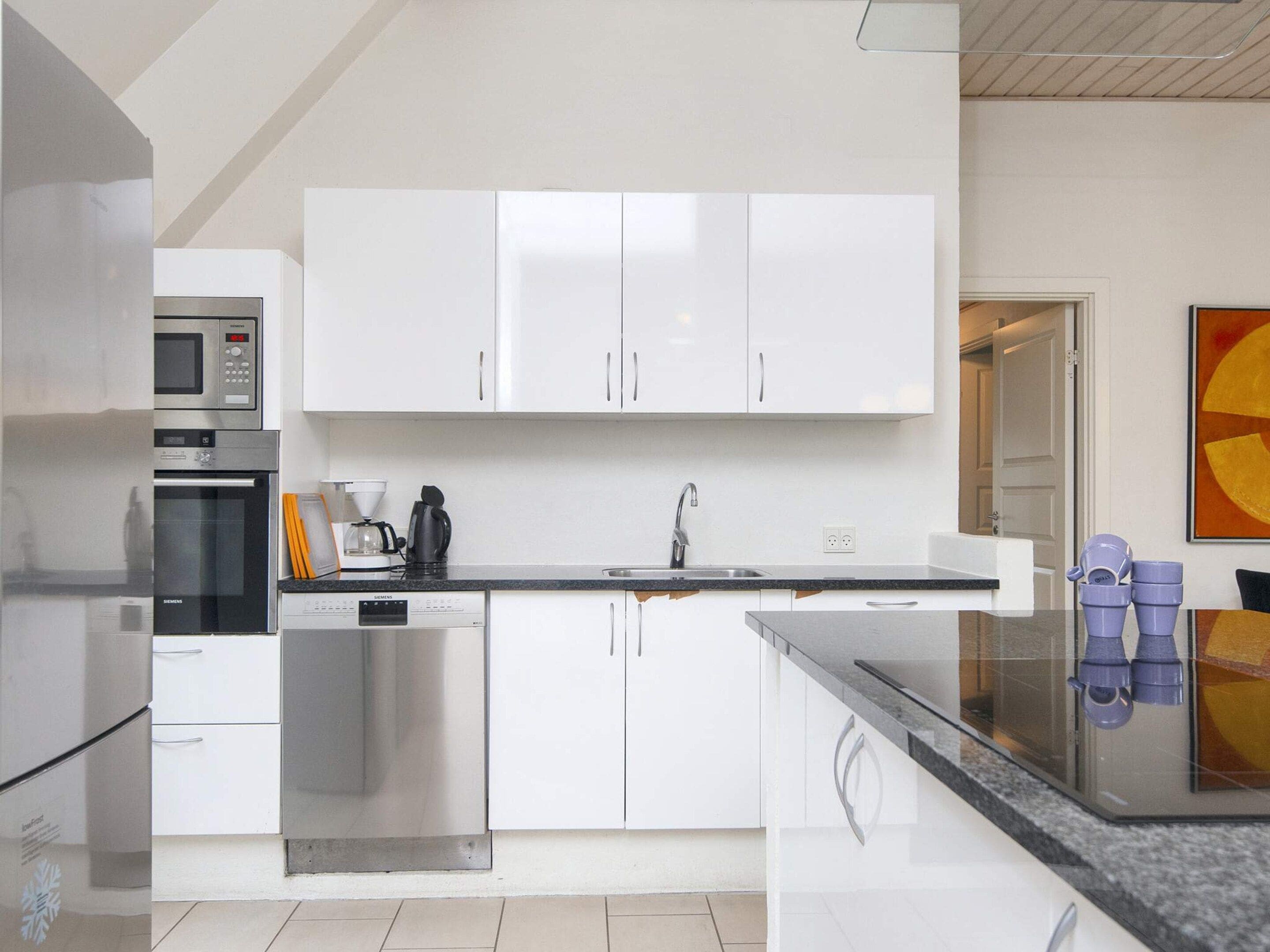 A modern kitchen with white cabinetry, a built-in oven, a coffee machine, and a sink.
