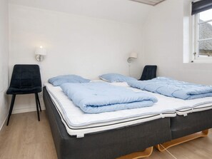 Ein Einzelbett mit schwarzem Gestell und einer Matratze, zwei Kissen, ein Nachttisch, ein Stuhl und ein Fenster mit Aussicht.