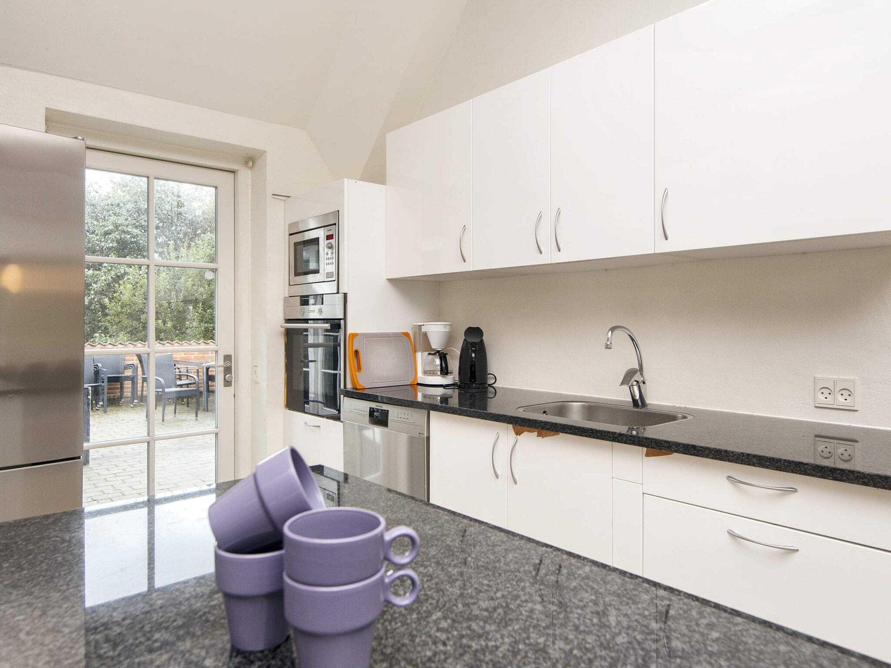 Eine moderne Küche mit weißen Schränken, einem Edelstahlkühlschrank, einer Mikrowelle und einer Kaffeemaschine.