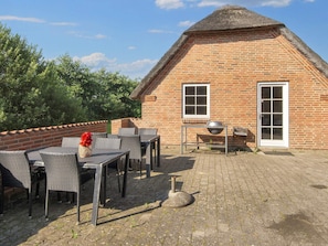 Een bakstenen gebouw met rieten dak, een tafel met stoelen en een barbecue buiten.