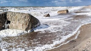 Un paysage côtier avec de gros rochers et une plage de sable sous un ciel nuageux.