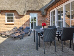 A patio with lounge chairs and a table, a thatched roof, brick walls, and a door. - 4 Star Holiday Home in Ulfborg (Ulfborg)