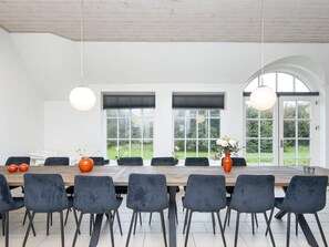 Een moderne eetruimte met een lange tafel, donkere stoelen en twee hangende lampen.