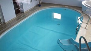 Una piscina rectangular techada con superficie de agua azul transparente, una escalera y un ventanal.
