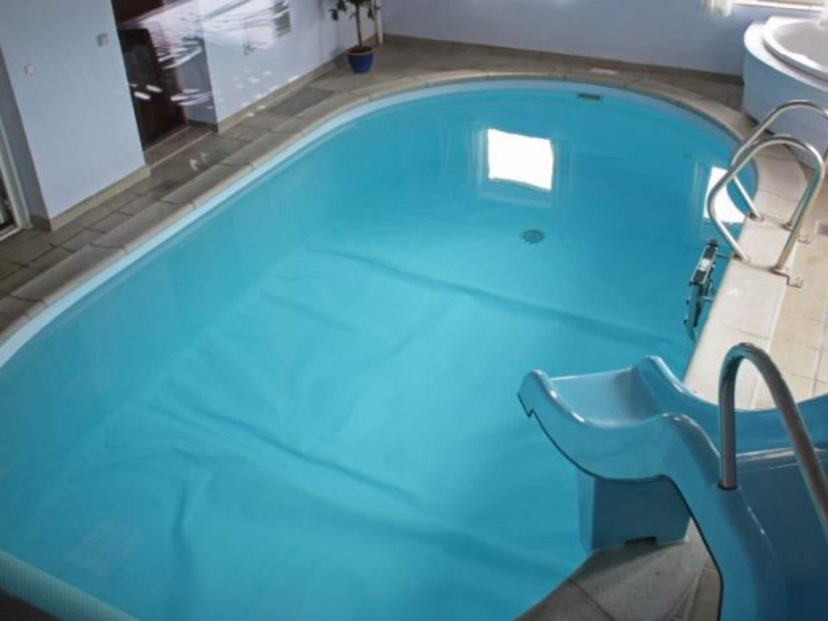 A rectangular swimming pool with a clear blue interior, a ladder, and a small window.