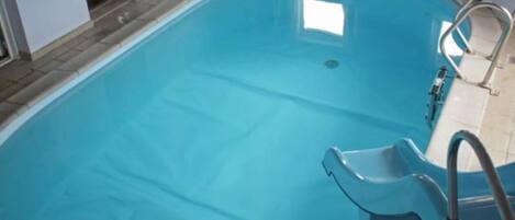A rectangular swimming pool with a clear blue interior, a ladder, and a small window.