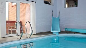 Una piscina interior con paredes de vidrio transparente, barandas de metal y un tobogán azul.