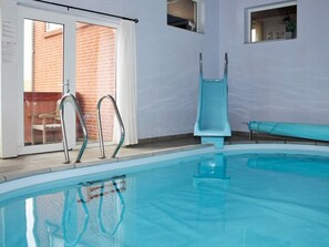 Ein Innenpool mit klaren Glasswänden, Metallhandläufen und einer blauen Rutsche.