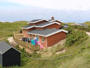 Ein zweigeschossiges Haus mit einer Terrasse, einer Rutsche und einem kleinen Schuppen.