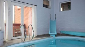 Una piscina con tobogán, puertas de cristal y vistas a un edificio de ladrillo.