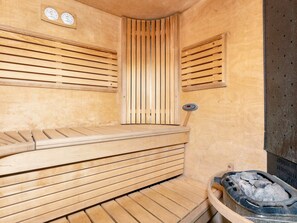 Eine Sauna mit Holzbänken, einer Steuerung und einem Steingrundschale.
