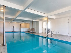 Ein großer, überdachter Swimmingpool mit klaren Glaswänden, einer Metallleiter und einem gefliesten Boden.