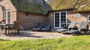 Un bâtiment en briques surmonté d’un toit de chaume, une enseigne indiquant « KILTYATT », et des sièges extérieurs avec des chaises et une table.