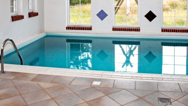 Une piscine dotée d’un sol carrelé, d’une échelle et de fenêtres ornées de motifs en forme de losanges.