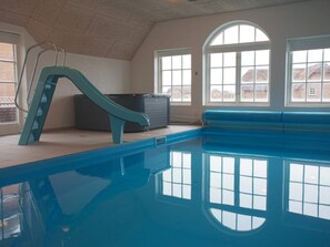 Piscina interior con tobogán, ventanas amplias y vista a casas desde el exterior.