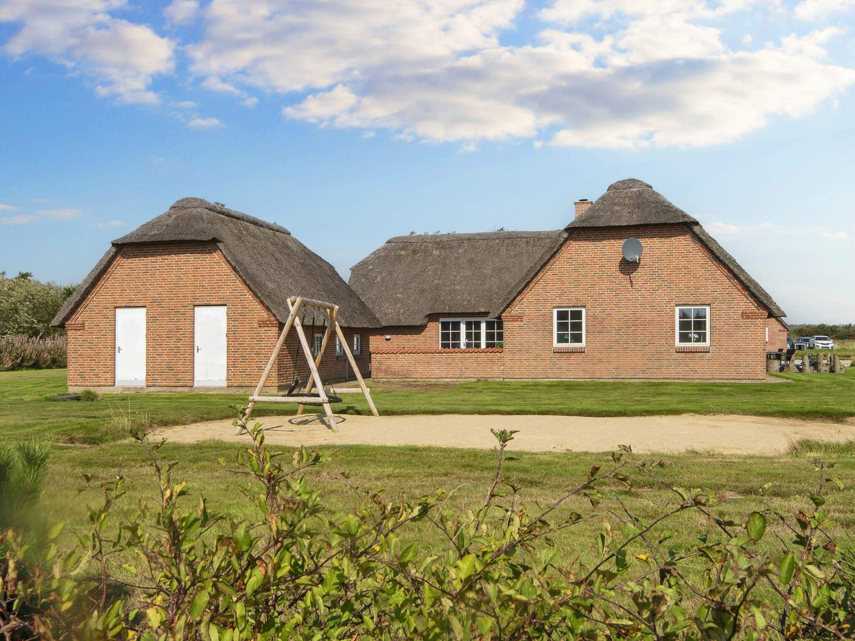 A brick building with a thatched roof, a swing set, and a grassy field.