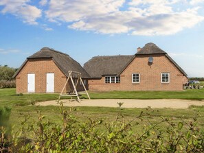 A brick building with a thatched roof, a swing set, and a grassy field. - 4 Star Holiday Home in Ulfborg (Ulfborg)