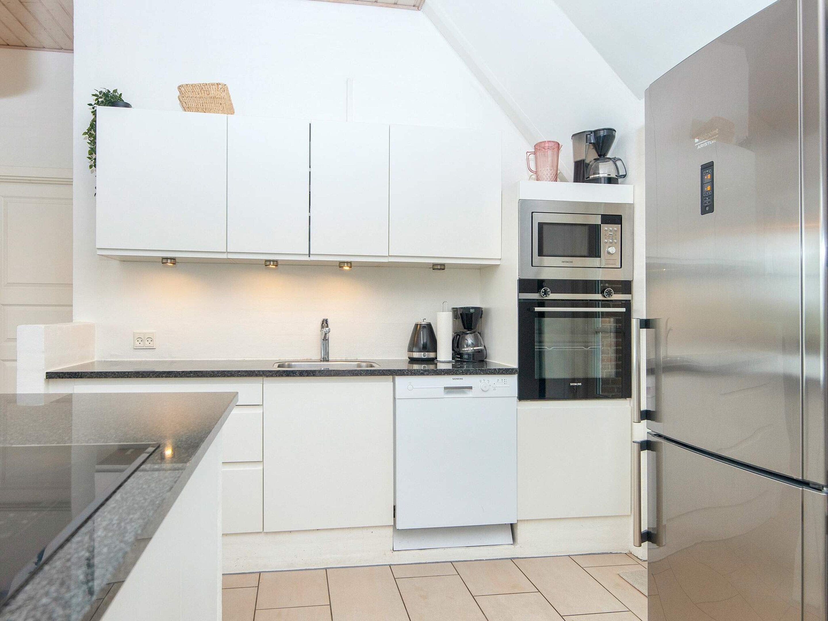 A modern kitchen with white cabinetry, a stainless steel refrigerator, a built-in oven, and a microwave.