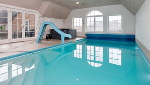 Una piscina interior con tobogán, amplias ventanas y una pared de ladrillo.