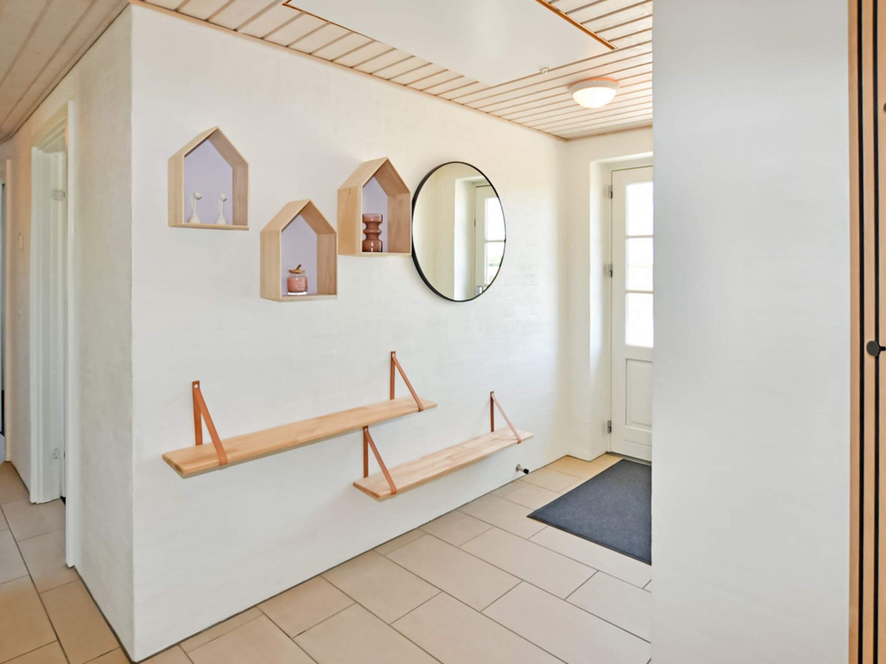 A hallway with a white wall, wooden beams on the ceiling, and a large mirror.