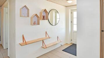 A hallway with a white wall, wooden beams on the ceiling, and a large mirror.