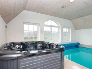 A hot tub in a room with a view of a swimming pool.