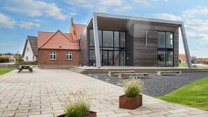 A modern building with a brick facade and large windows, a paved walkway, and two square planters with grass. - 4 Star Holiday Home in Harboore (Harboore)