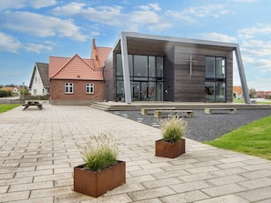 Ein modernes Gebäude mit Ziegelaußenwand und großen Fenstern, ein gepflasterter Weg und zwei quadratische Pflanzkästen mit Gras.