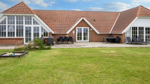 A brick house with a tiled roof, large windows, and a patio area with outdoor furniture. - 4 Star Holiday Home in Harboore (Harboore)