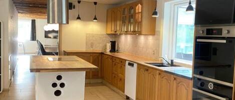 A modern kitchen with wooden cabinets, a central island, stainless steel appliances, and pendant lighting.