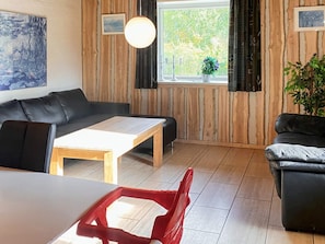A room with a wooden wall, a black leather sofa, a wooden coffee table, and a window with curtains. - 4 Star Holiday Home in Karup J (Karup)