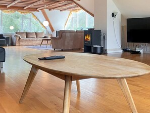 A modern living room with a wooden table, a sofa, a TV, and a wood-burning stove. - 4 Star Holiday Home in Karup J (Karup)