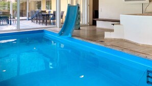 Una piscina con tobogán, una tumbona y vistas a un área de comedor al aire libre.
