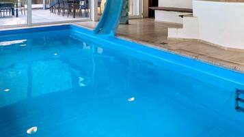 Una piscina con tobogán, una tumbona y vistas a un área de comedor al aire libre.
