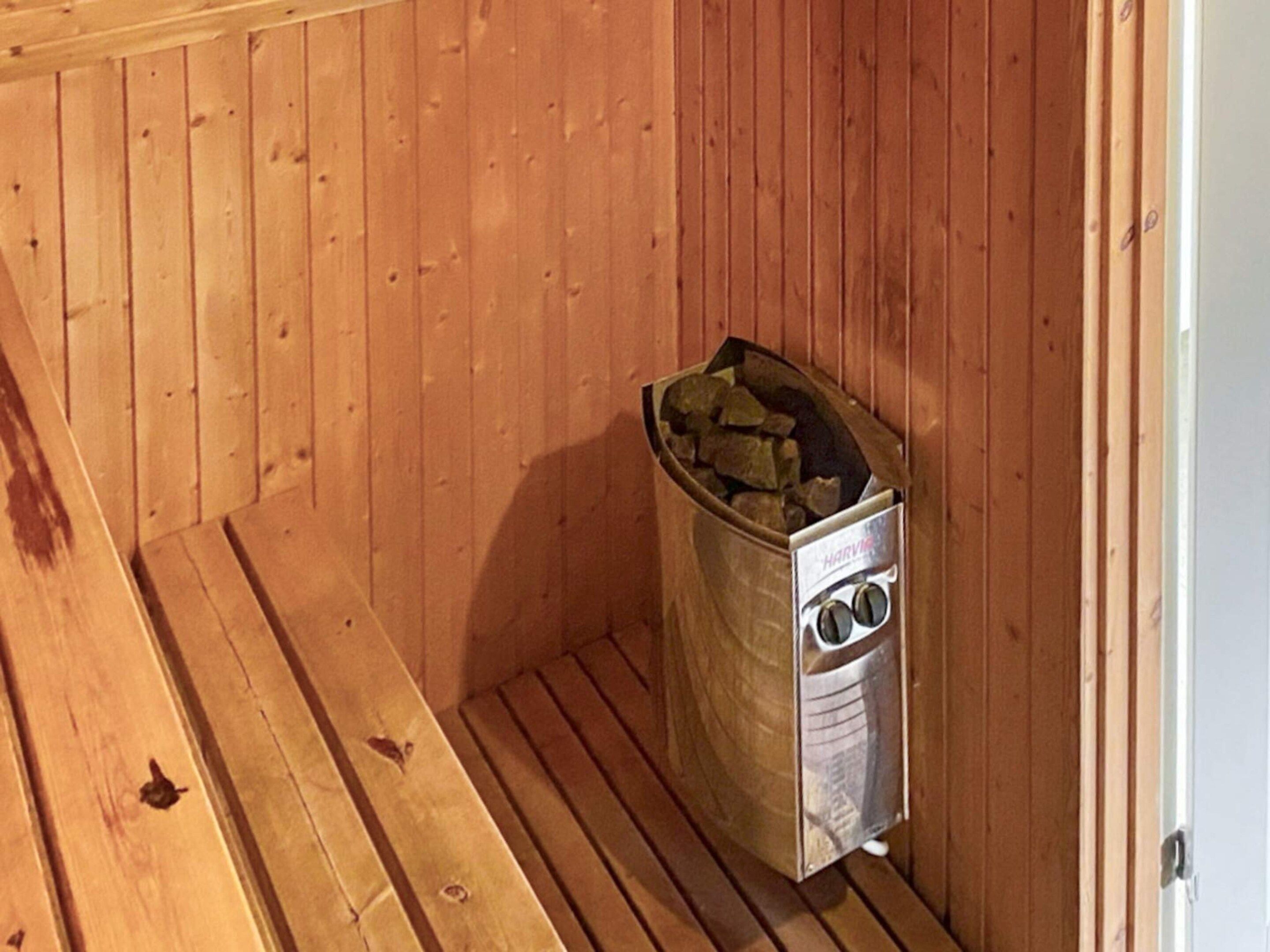 A sauna room with wooden walls and a floor, a sauna heater, and a trash bin.