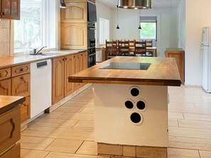 A modern kitchen with wooden cabinets, a central island with a built-in sink, and a dining area with wooden chairs.