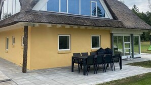 Una casa con techo de paja, paredes exteriores amarillas y un patio con mobiliario exterior.