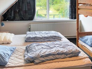 A dormitory room with bunk beds, a window with curtains, a radiator, and a bed with a quilted mattress. - 4 Star Holiday Home in Karup J (Karup)