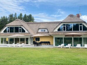 A two-story house with a thatched roof, large windows, and a covered patio area with outdoor seating. - 4 Star Holiday Home in Karup J (Karup)