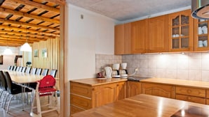 A modern kitchen with wooden cabinets, a dining table with chairs, and a built-in stove. - 4 Star Holiday Home in Karup J (Karup)