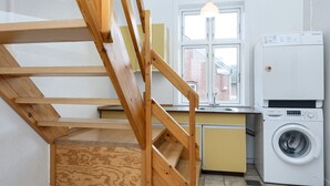 A kitchen with a wooden staircase, a washing machine, and a window with a view of a brick building. - 18 Person Holiday Home in Skjern (Skjern)