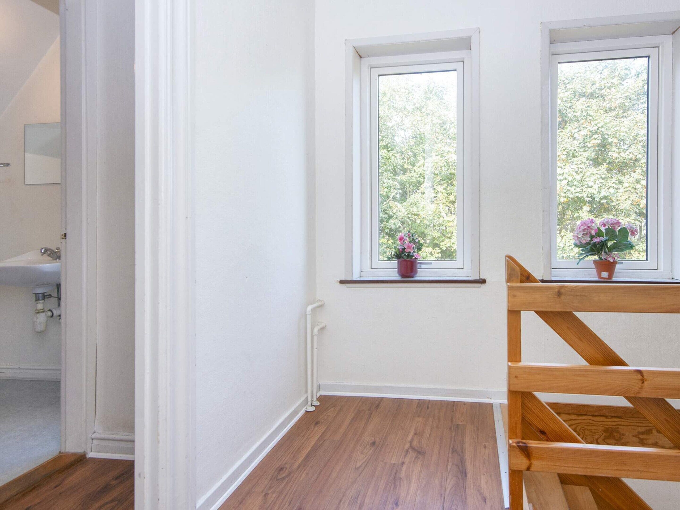 A room with two windows, a wooden bench, and a potted plant on the windowsill.