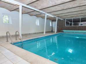 Una piscina interior con suelo de baldosas, pared de ladrillo y techo blanco.