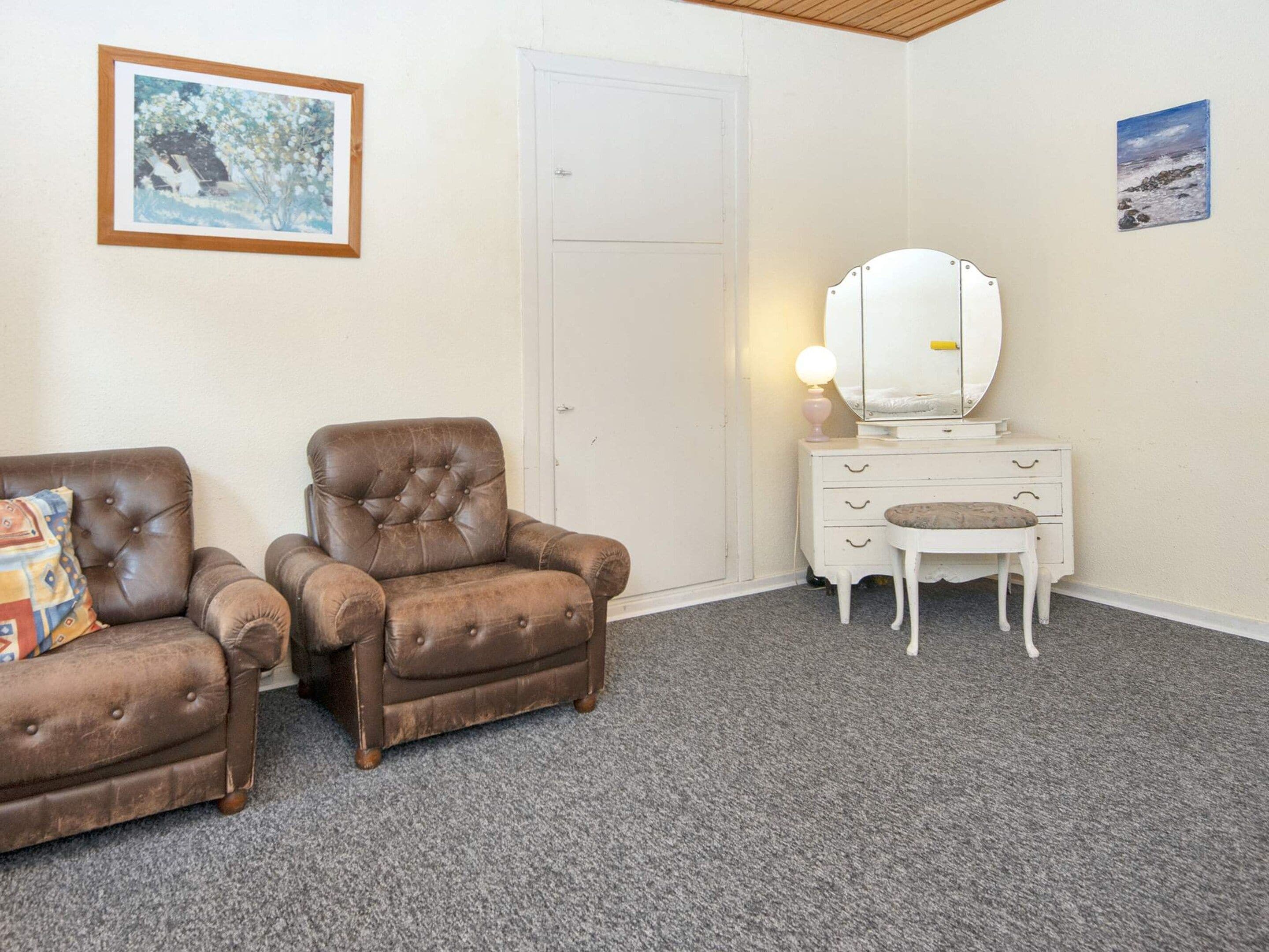 A room with two brown leather armchairs, a white dresser with a mirror, and a framed picture on the wall.