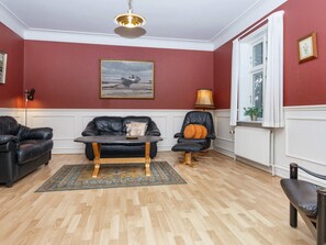 A room with a red wall, a black leather sofa, a wooden coffee table, a black leather armchair, and a floor lamp. - 18 Person Holiday Home in Skjern (Skjern)