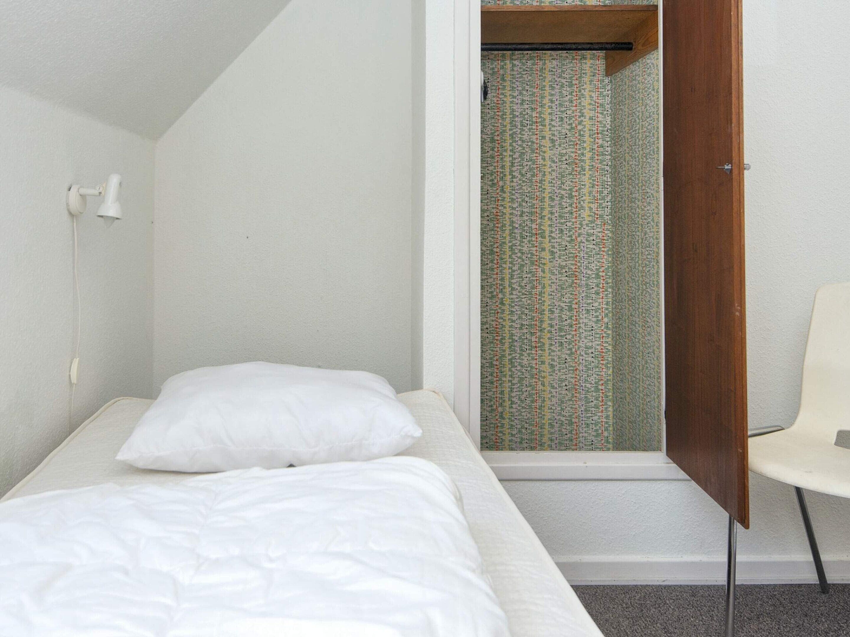 Une petite chambre avec un lit simple, dotée d’une porte en bois donnant sur une salle de bain dont les murs sont recouverts d’un papier peint à motifs.