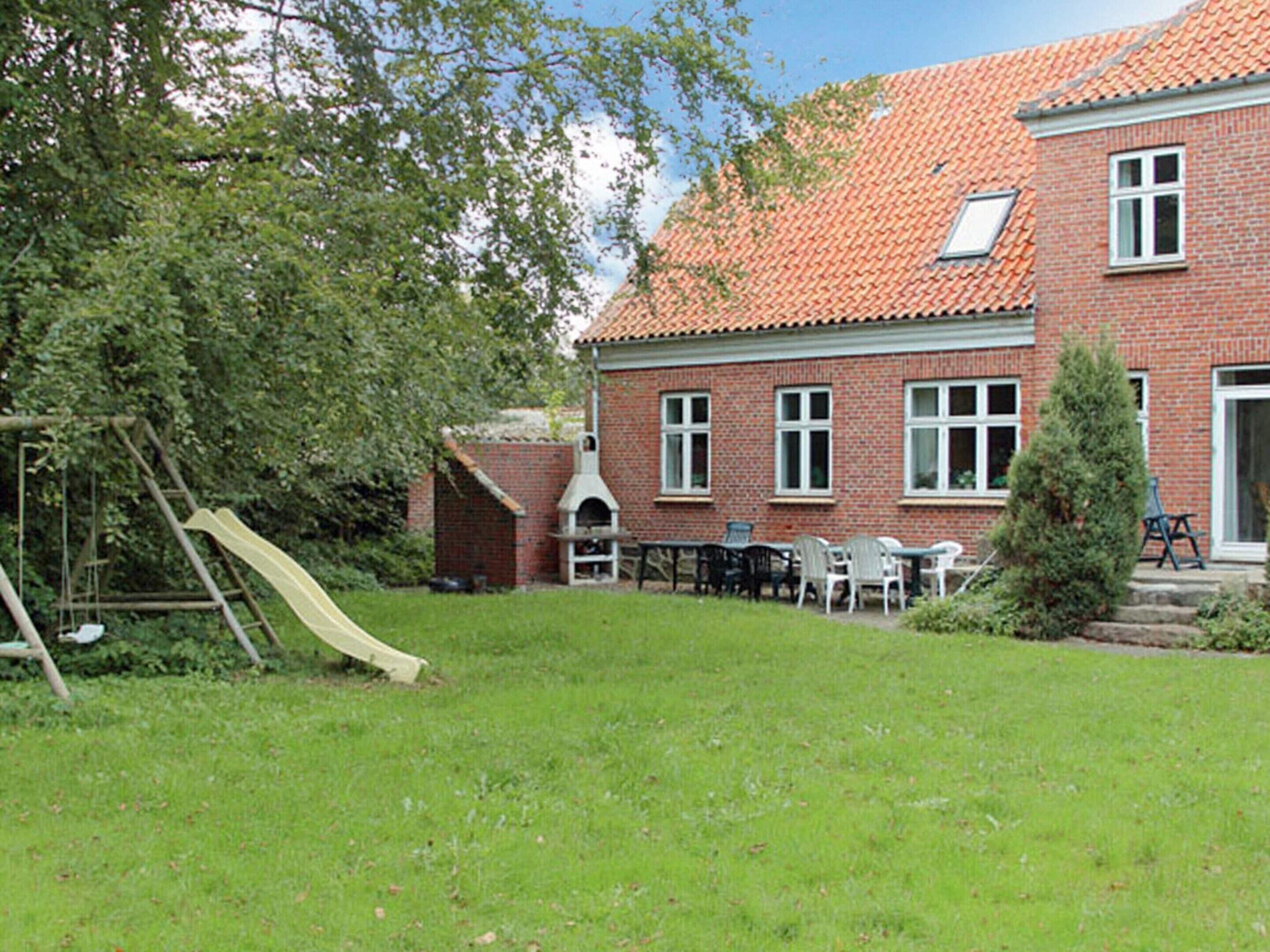 Une maison en briques avec un toit en tuiles, un toboggan et un espace de détente extérieur.