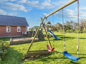 A playground with swings and a slide, a brick house, and a grassy yard. - 4 Star Holiday Home in Thyholm (Thyholm)
