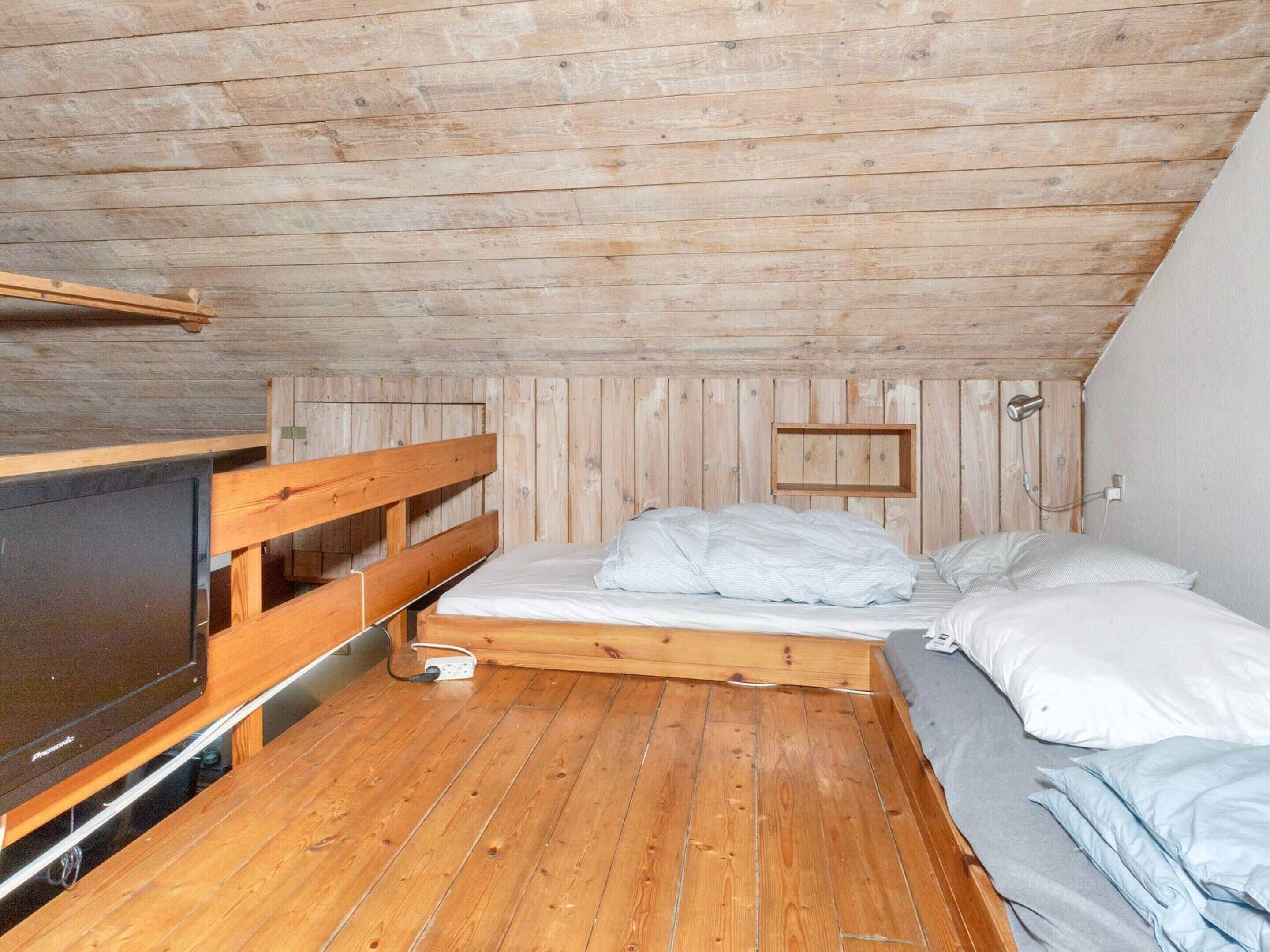 Een kleine kamer met houten lambrisering, een bed, een televisie en een stopcontact op de vloer.